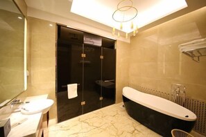Un baño moderno con encimera de mármol, bañera negra y ducha con mampara de vidrio.