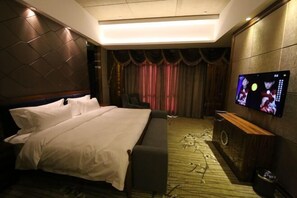 A hotel room with a bed, a TV on the wall, a small seating area, and a curtain backdrop. - Jinchang Hotel (Jinchang)