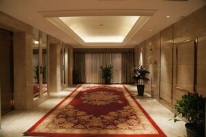 Un pasillo de hotel con alfombra roja, plantas en macetas y un muro espejado.