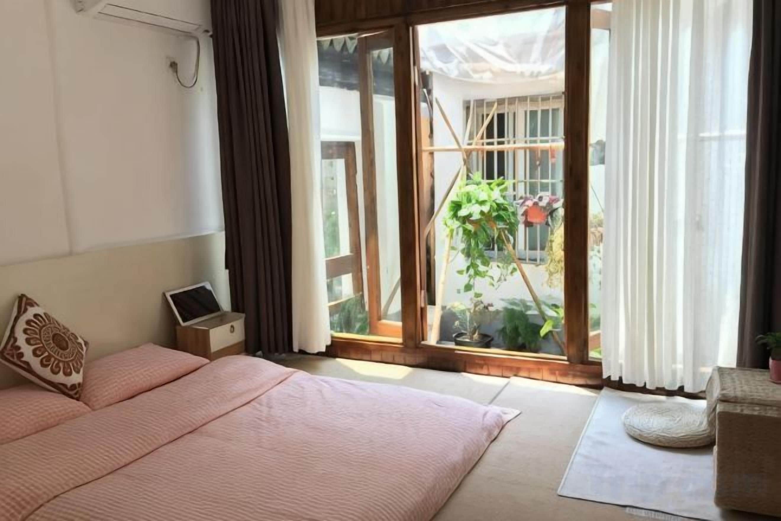 Un dormitorio con una cama, una computadora portátil, una ventana con cortinas y vistas a un jardín.