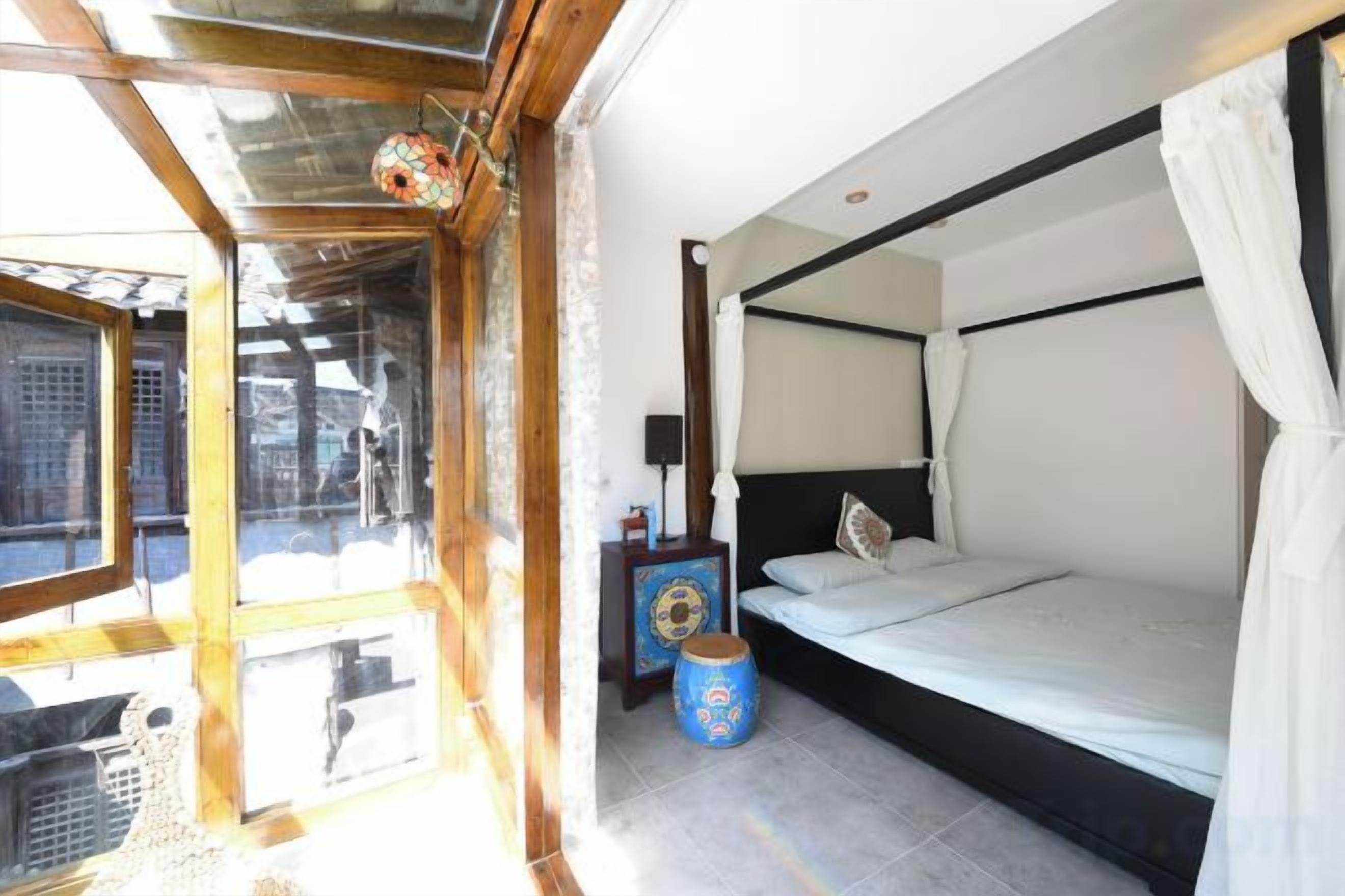 A bedroom with a bed, a window, and a small table with a lamp.