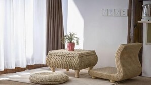 A room with a woven ottoman, a chair, a small table with a plant, and a power outlet on the wall. - Tongli Jizhu Inn (Suzhou)