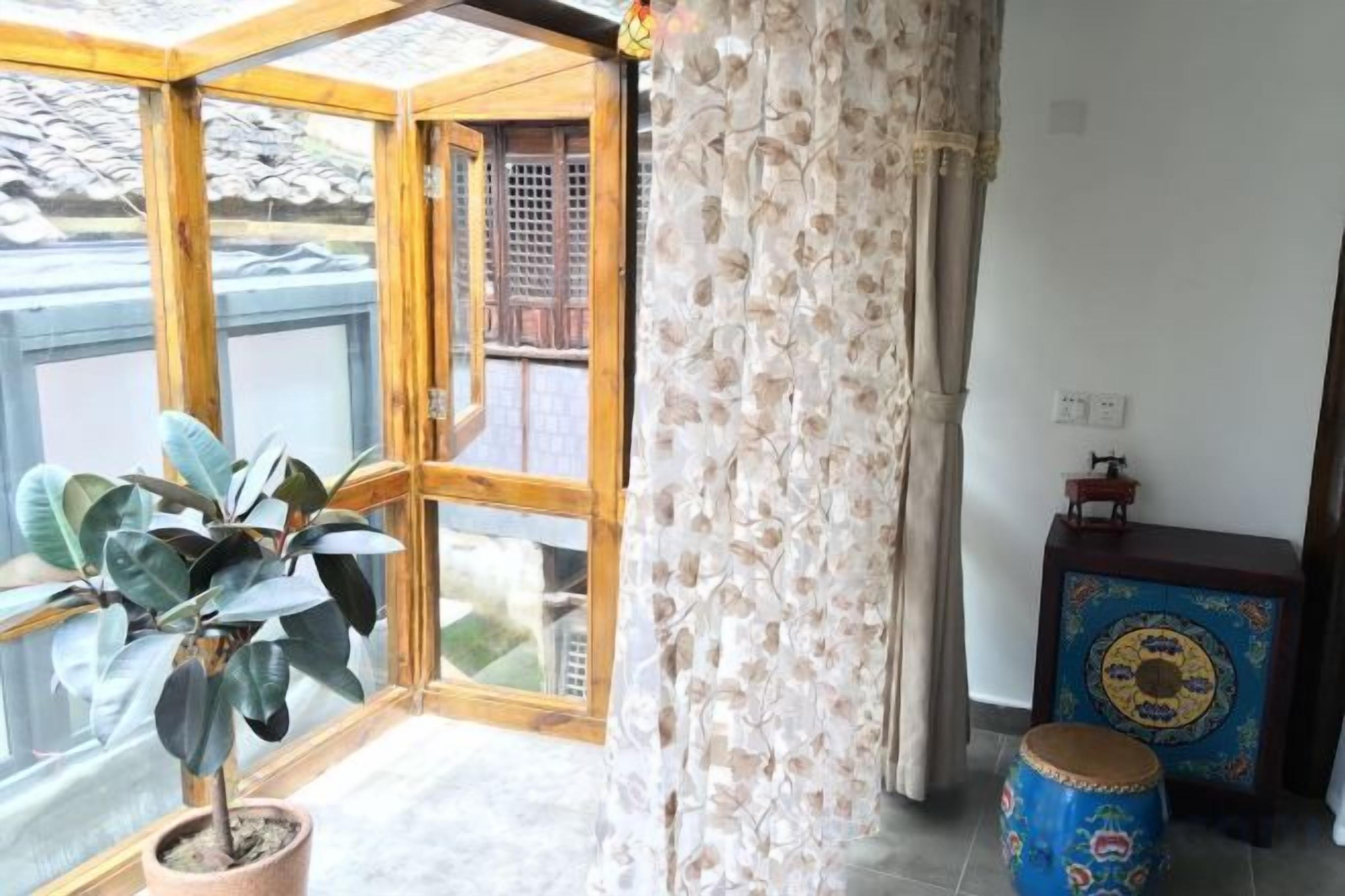 A room with a large window, a potted plant, a decorative drum, and a small table with a decorative item.