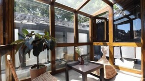 A sunlit room with a glass ceiling, a woven chair, a small table, and a potted plant. - Tongli Jizhu Inn (Suzhou)