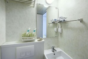 Une salle de bain avec un lavabo blanc, un miroir et une étagère sur laquelle se trouvent des brosses à dents et un gobelet.