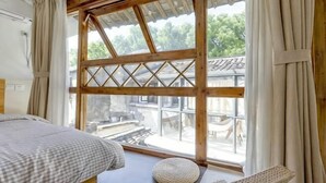 A room with a bed, a round woven chair, a large window with wooden frames, and a view of a traditional building outside. - Tongli Jizhu Inn (Suzhou)