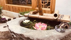 A stone pond with a pink lotus flower, bamboo structures, and a small bridge. - Tongli Jizhu Inn (Suzhou)