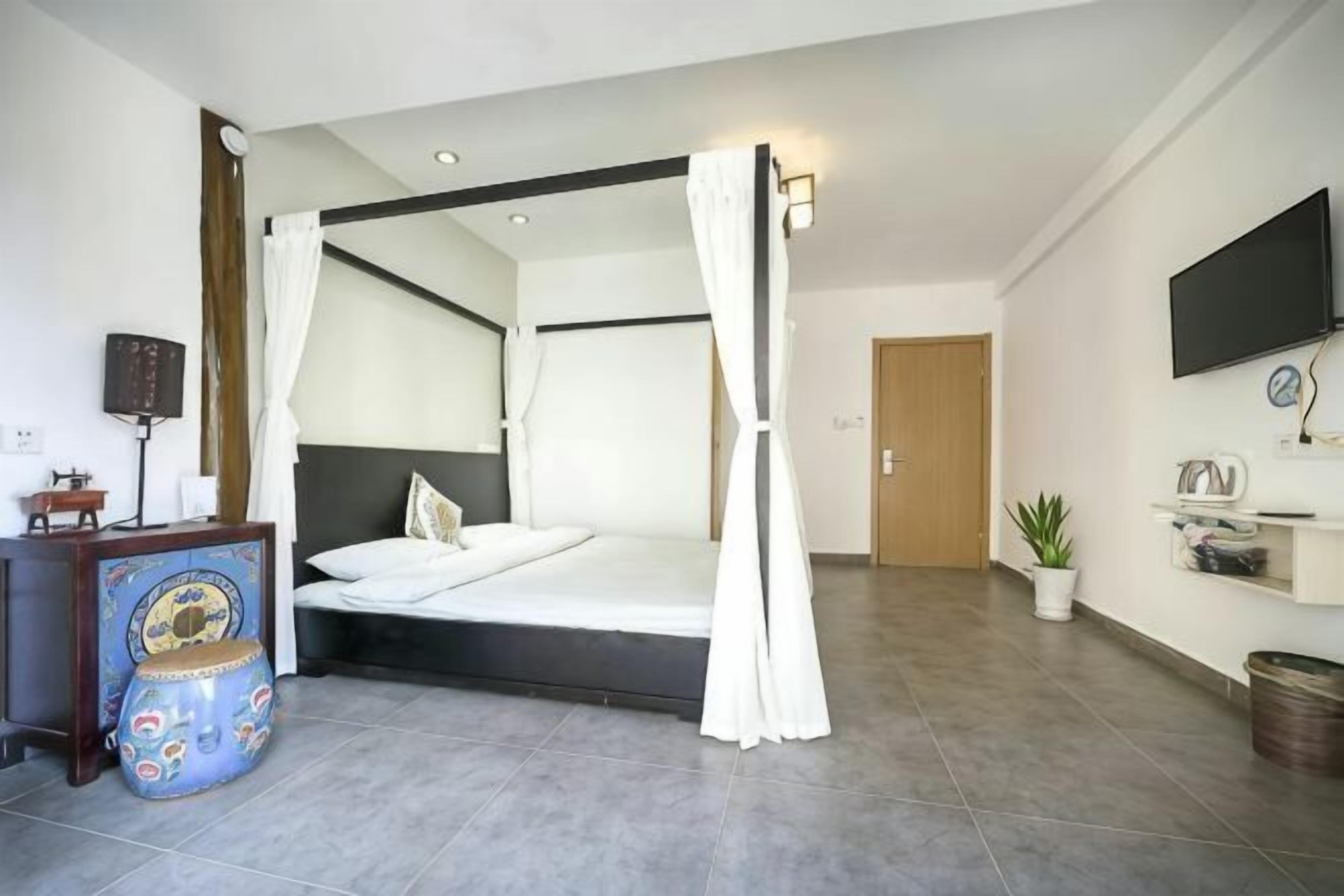 A bedroom with a four-poster bed, a bedside table, a television, and a potted plant.