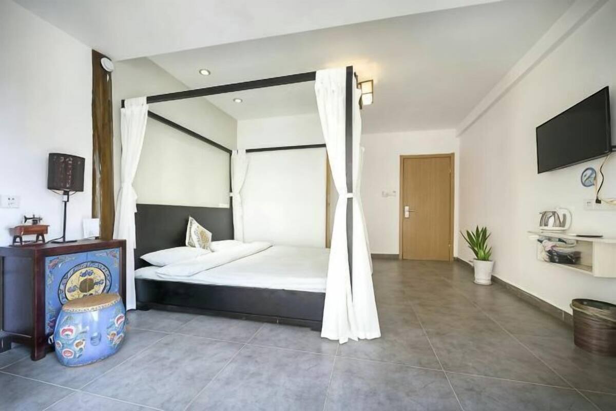 Un dormitorio con cama con dosel, una mesita de noche, un televisor y una planta en maceta.