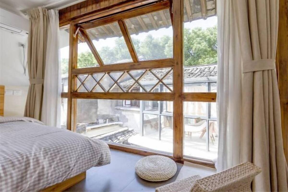 Una habitación con una cama, un taburete redondo tejido y una ventana grande con un diseño de celosía de madera.