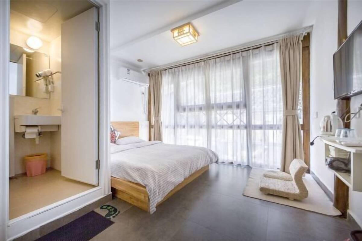 Un dormitorio con cama, mesita de noche, televisión y ventana con cortinas.