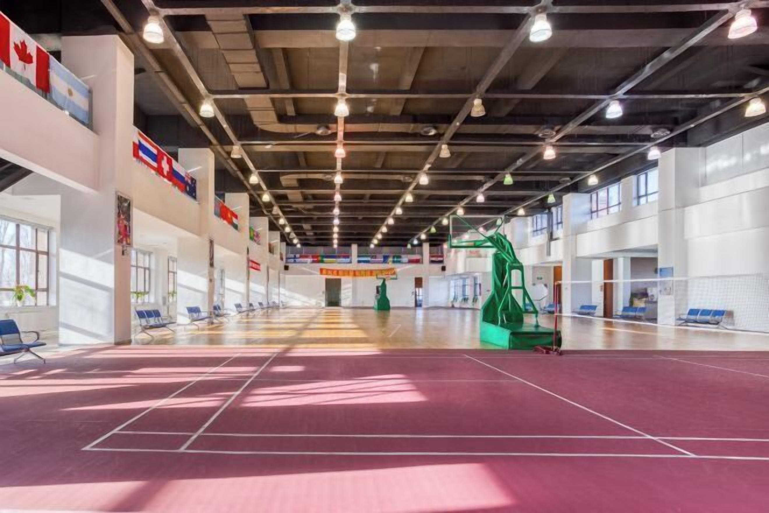 A spacious indoor area with a basketball court, seating, and flags on the walls.