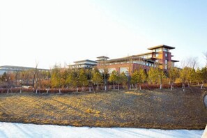A multi-story building with a modern architectural design, surrounded by a landscaped area with trees and a snow-covered ground. - Lianhuashan International Business Center (Changchun)