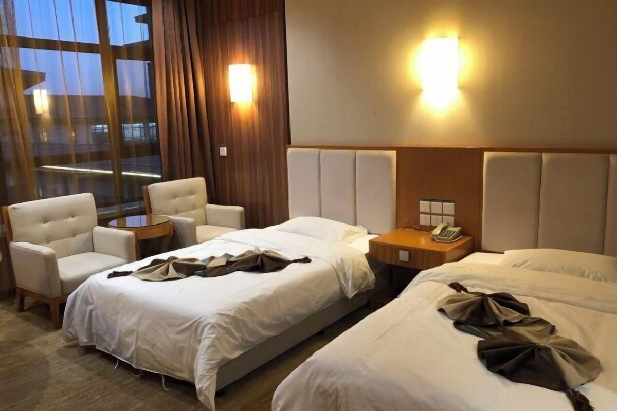 A hotel room with two beds, a chair, a small table, and a window with curtains.