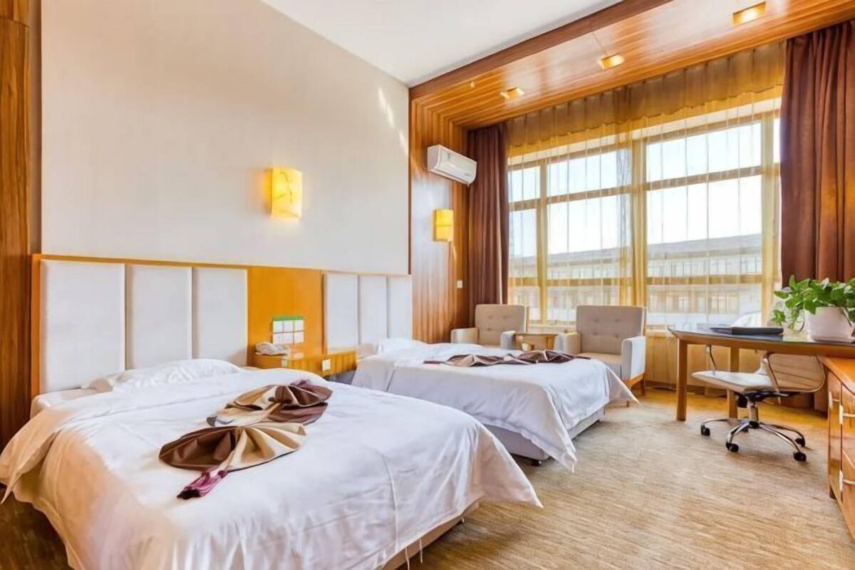 A hotel room with two beds, a desk, a chair, and a large window.