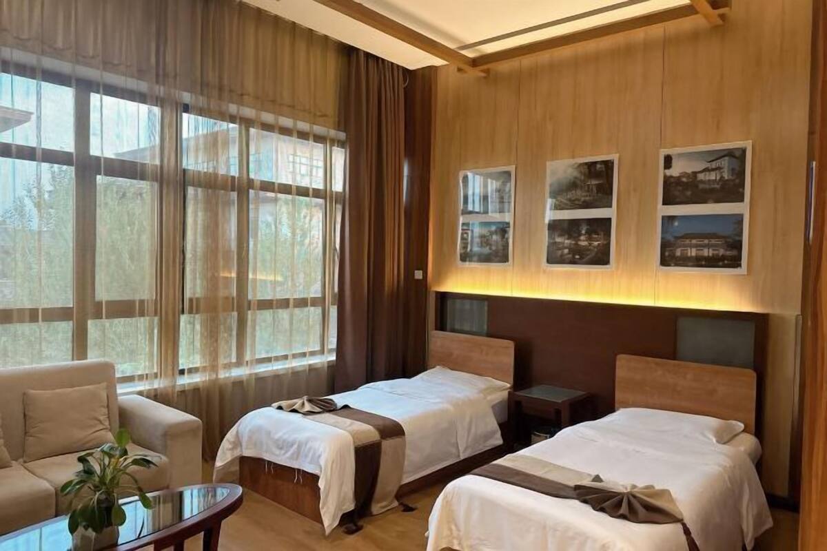 A hotel room with two beds, a sofa, a table, and a large window with curtains.