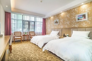 Habitación de hotel con dos camas, un escritorio y sillas. Amplias ventanas con cortinas, alfombra estampada y decoración en las paredes.
