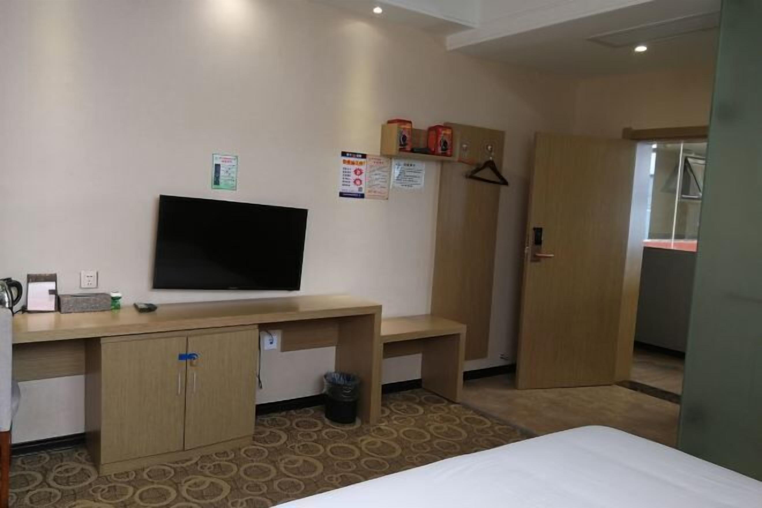 Habitació d'hotel amb llit, escriptori amb televisió, armari i porta que dona a una altra habitació.