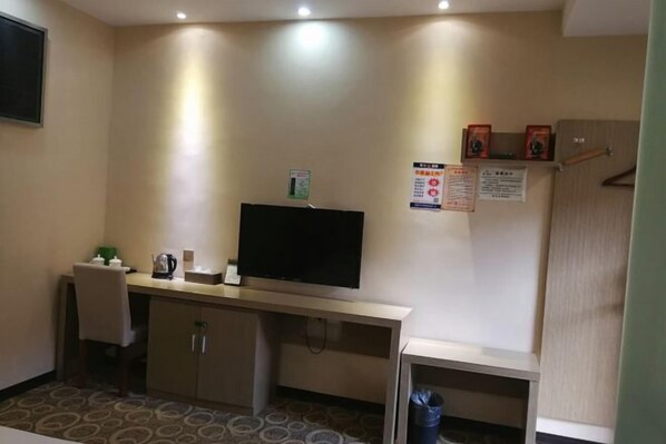 Habitación de hotel con escritorio, televisión y un mueble pequeño. Se observan carteles en la pared y un perchero.