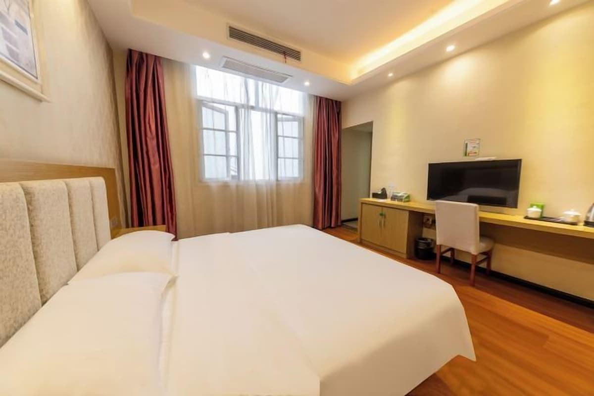 Habitación de hotel con cama, escritorio, silla, televisión y ventana con cortinas.