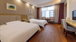 Habitación de hotel con dos camas, un escritorio, una silla y una ventana con cortinas.