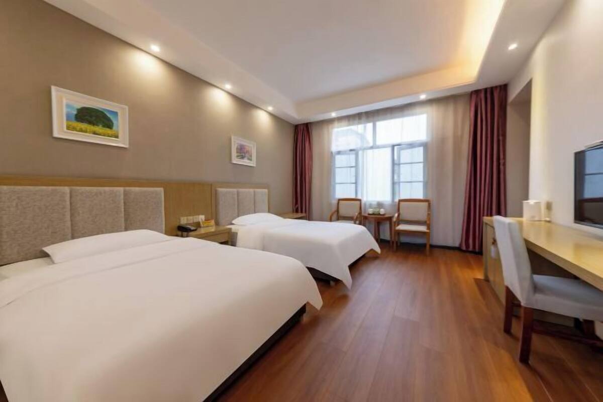 A hotel room with two beds, a desk, a chair, and a window with curtains.