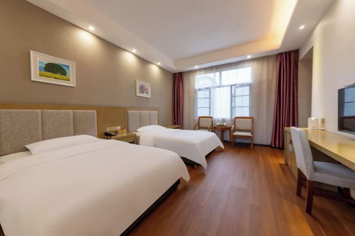 Habitación de hotel con dos camas, un escritorio, una silla y una ventana con cortinas.