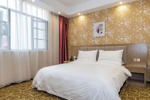 Una habitación de hotel con una cama grande, una mesita de noche, un reloj de pared y una ventana con cortinas translúcidas.