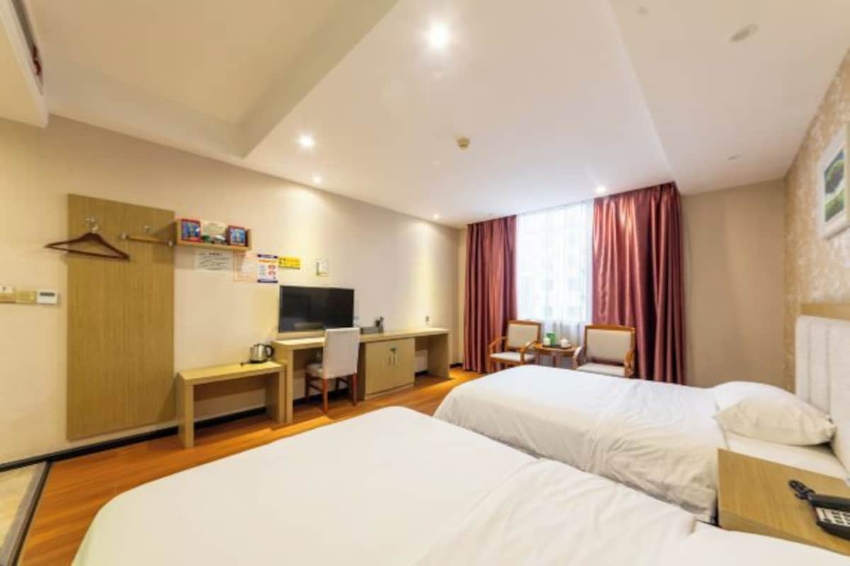 Una habitación de hotel con dos camas, un escritorio, un televisor y una ventana con cortinas.