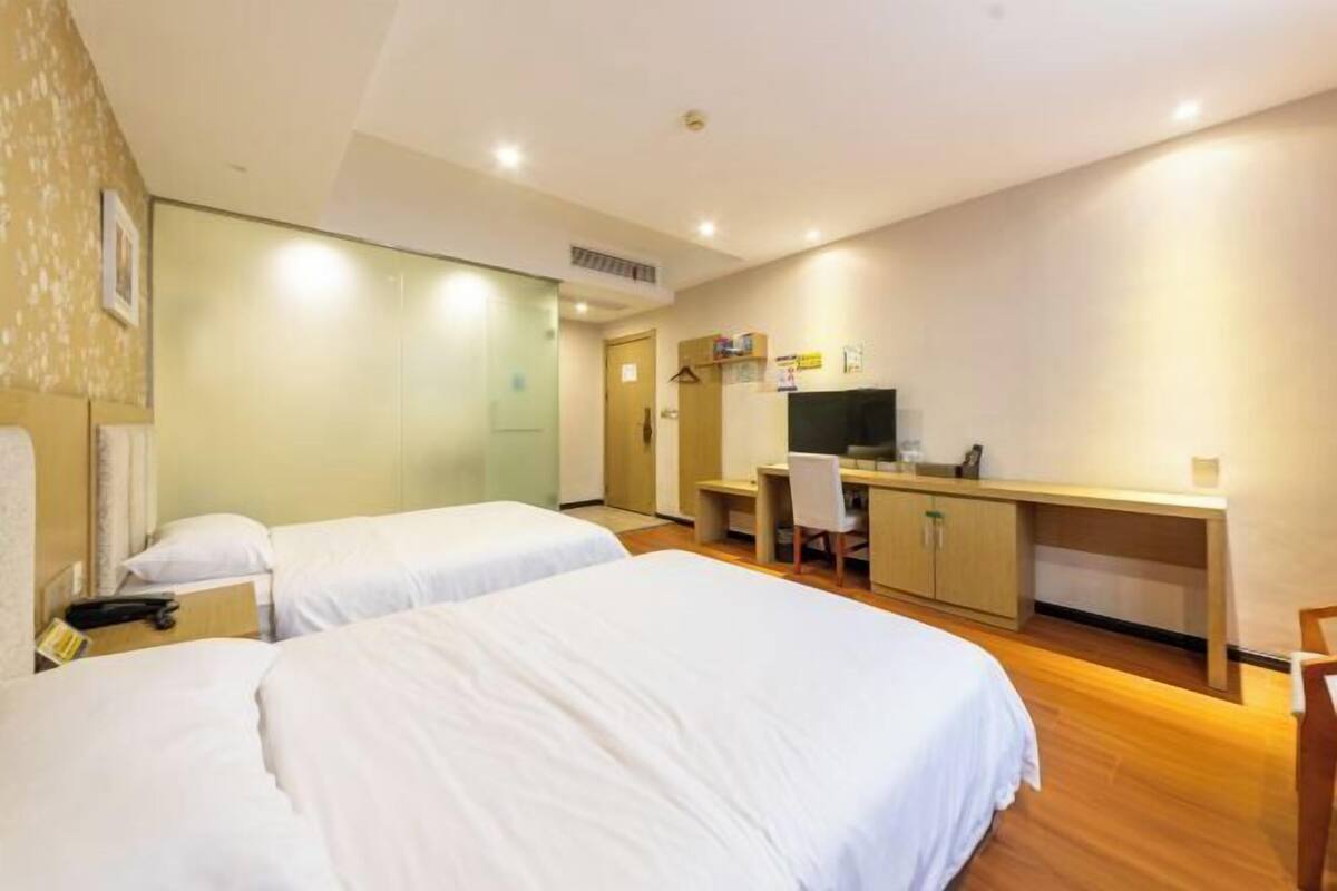 A hotel room with two beds, a desk, a chair, a TV, and a wardrobe.