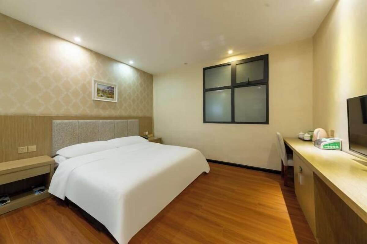 A hotel room with a bed, bedside table, TV, and a window.