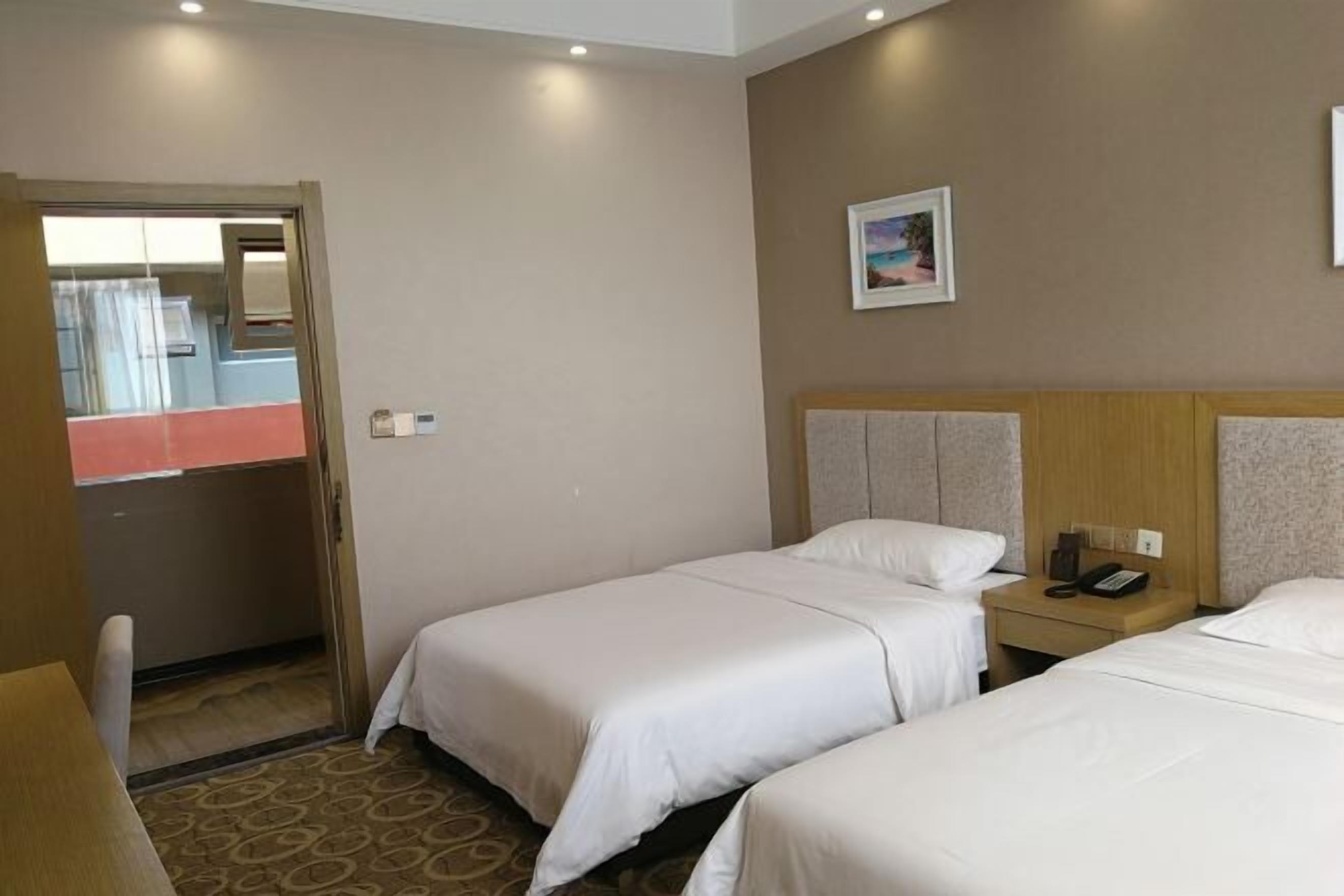 A hotel room with two beds, a wooden headboard, a bedside table with a phone, and a framed picture on the wall.