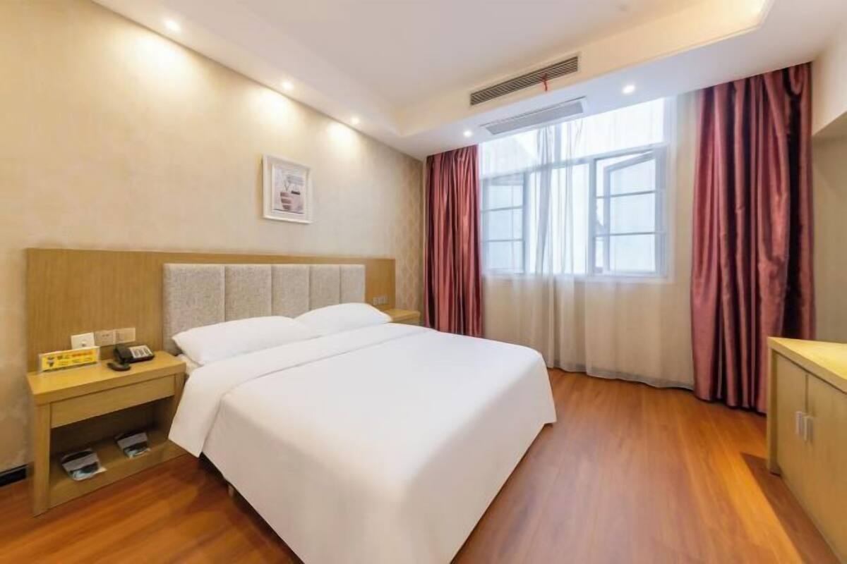 A hotel room with a bed, nightstand, and a window with curtains.