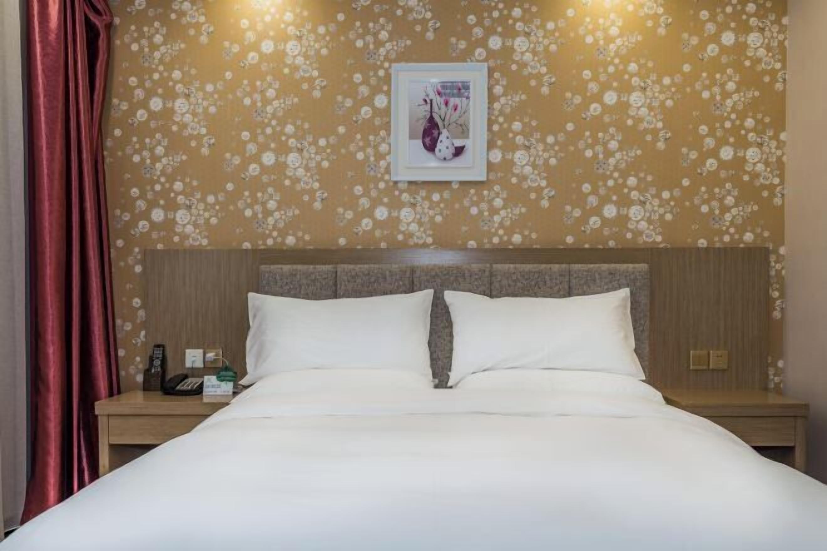 A hotel room with a bed, a nightstand, a telephone, and a framed picture on the wall.