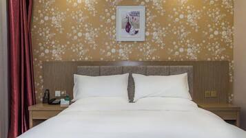 A hotel room with a bed, a nightstand, a telephone, and a framed picture on the wall.