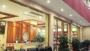 Een hotellobby met een receptiebalie, zithoek en potplanten.