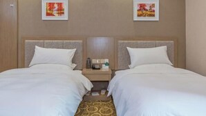 Een hotelkamer met twee bedden, een nachtkastje met een lamp en twee ingelijste foto’s aan de muur.