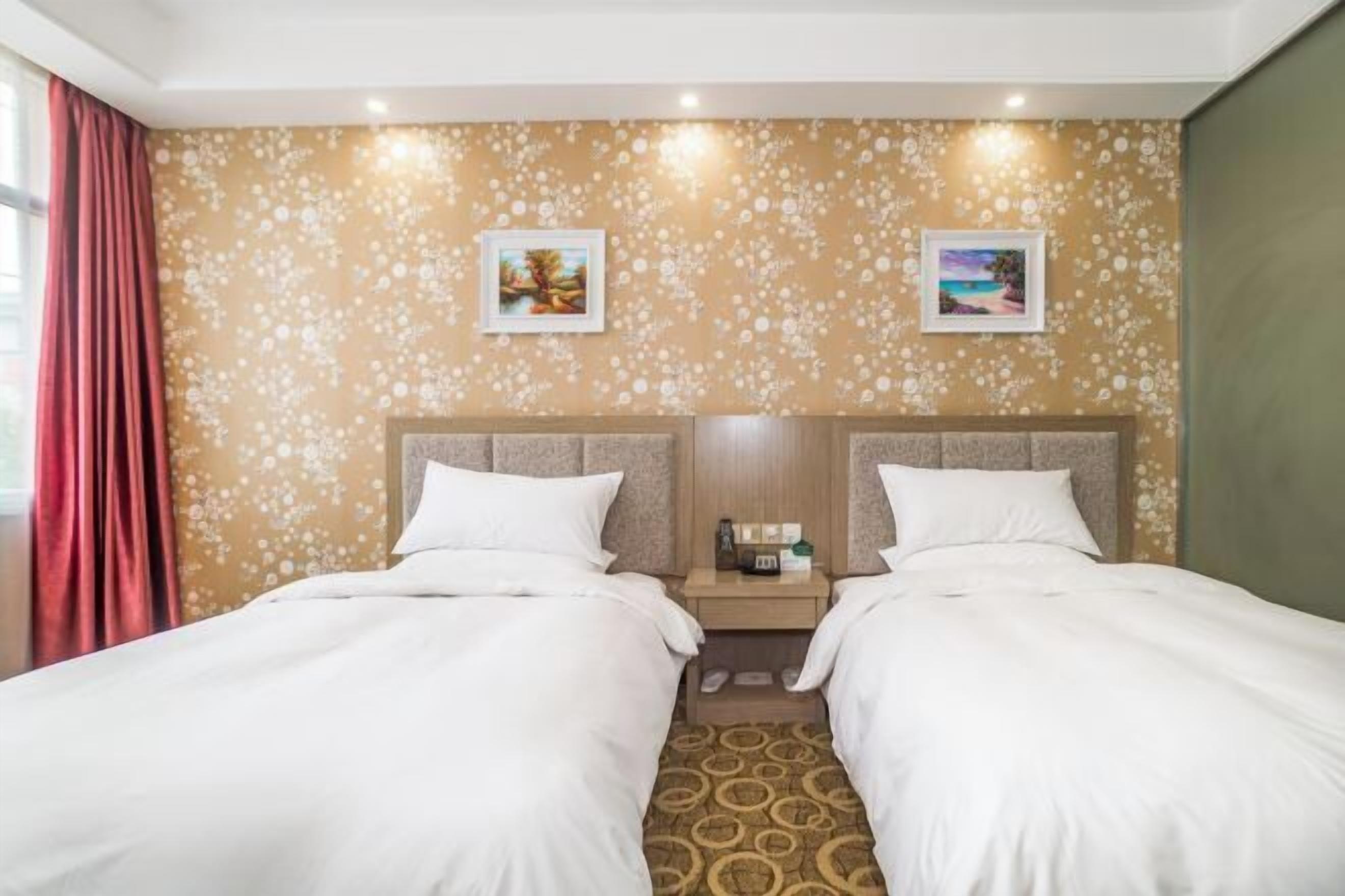 A hotel room with two beds, a nightstand with a lamp, and floral wallpaper.