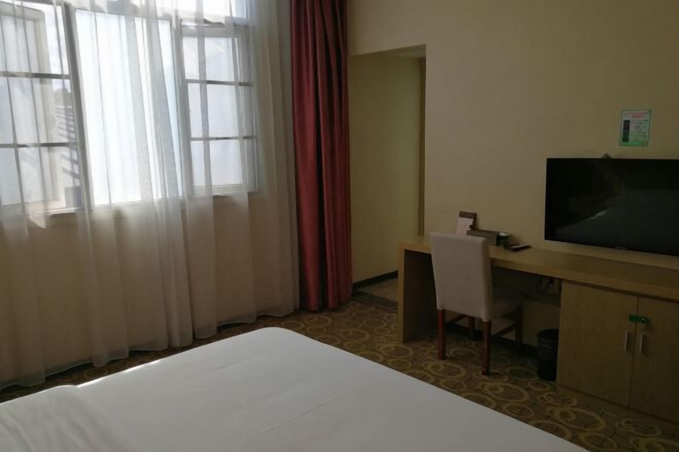 A hotel room with a bed, a desk, a chair, a television, and a window with curtains.