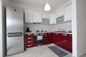 Eine moderne Küche mit weißen Schränken, einer roten Arbeitsplatte, einem eingebauten Backofen und einer Hängeleuchte.