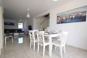 A dining area with a white table and chairs, a painting on the wall, and a staircase leading to another room.