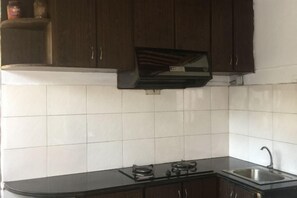 A kitchen with dark wooden cabinets, a gas stove, and a stainless steel sink. - Bishan Zhoujiayuan Farmhouse (Yi County)