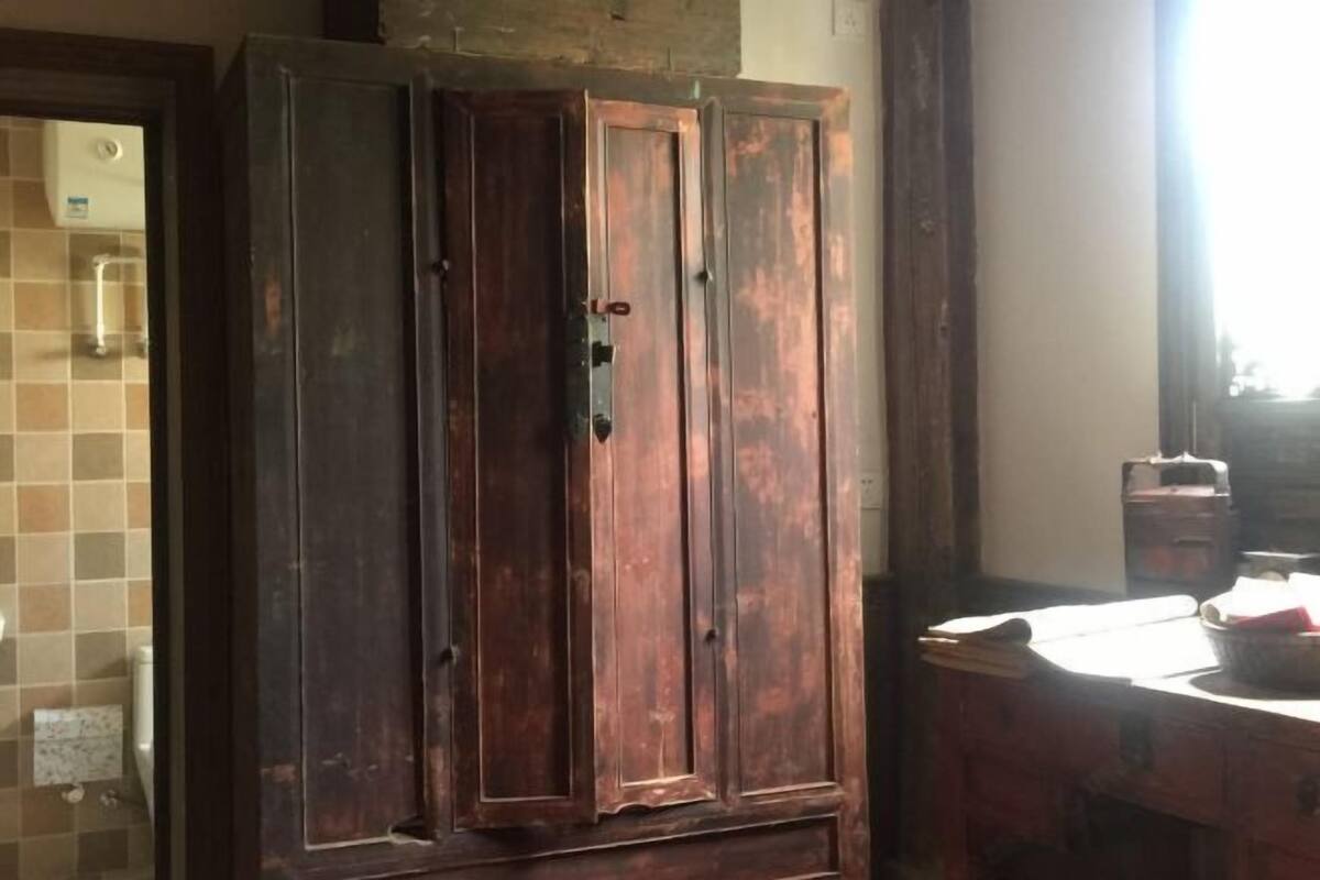 A wooden wardrobe with two doors, a tiled wall, and a small table with items on it.