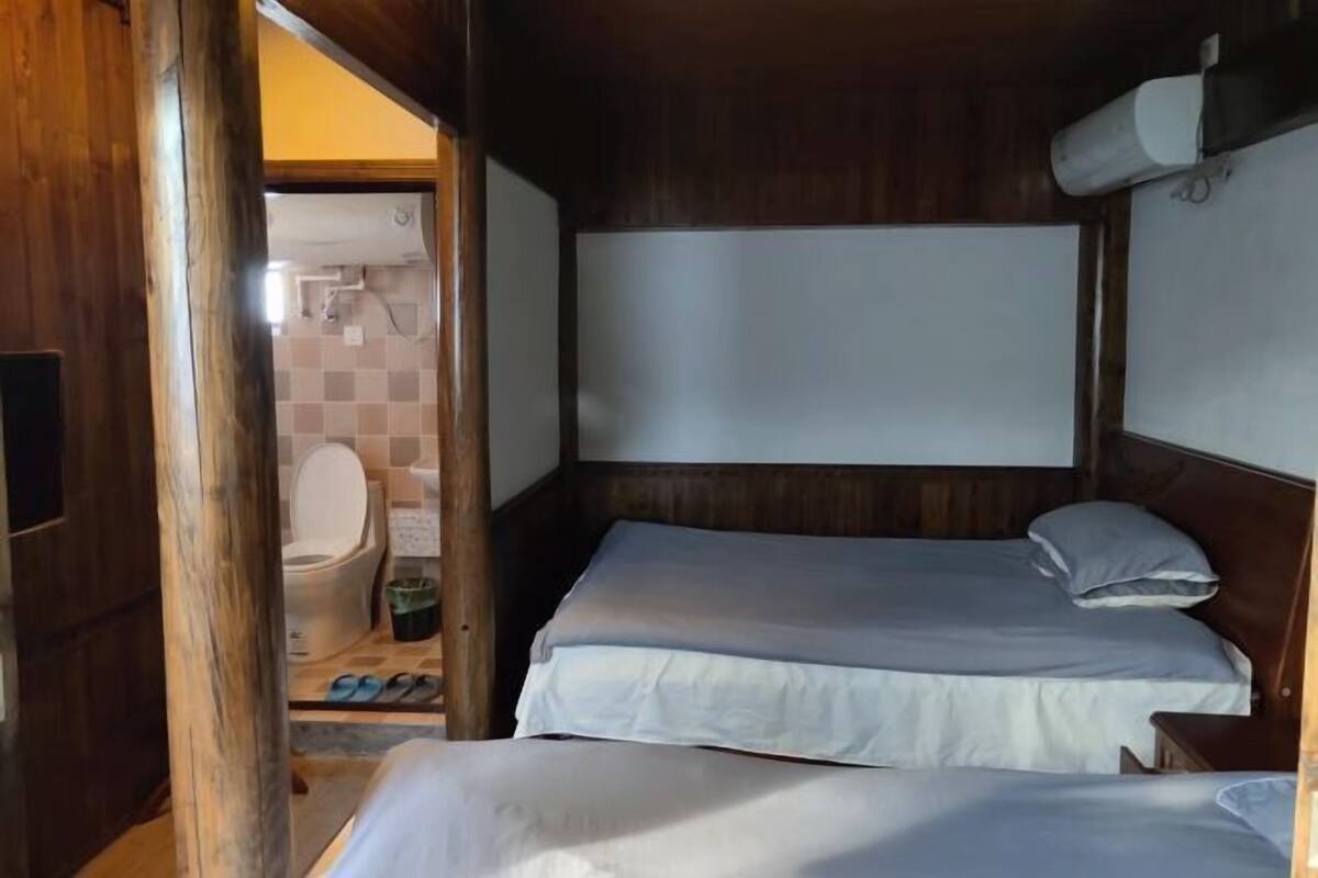 A small, wooden room with two beds, a toilet, and a shower area.
