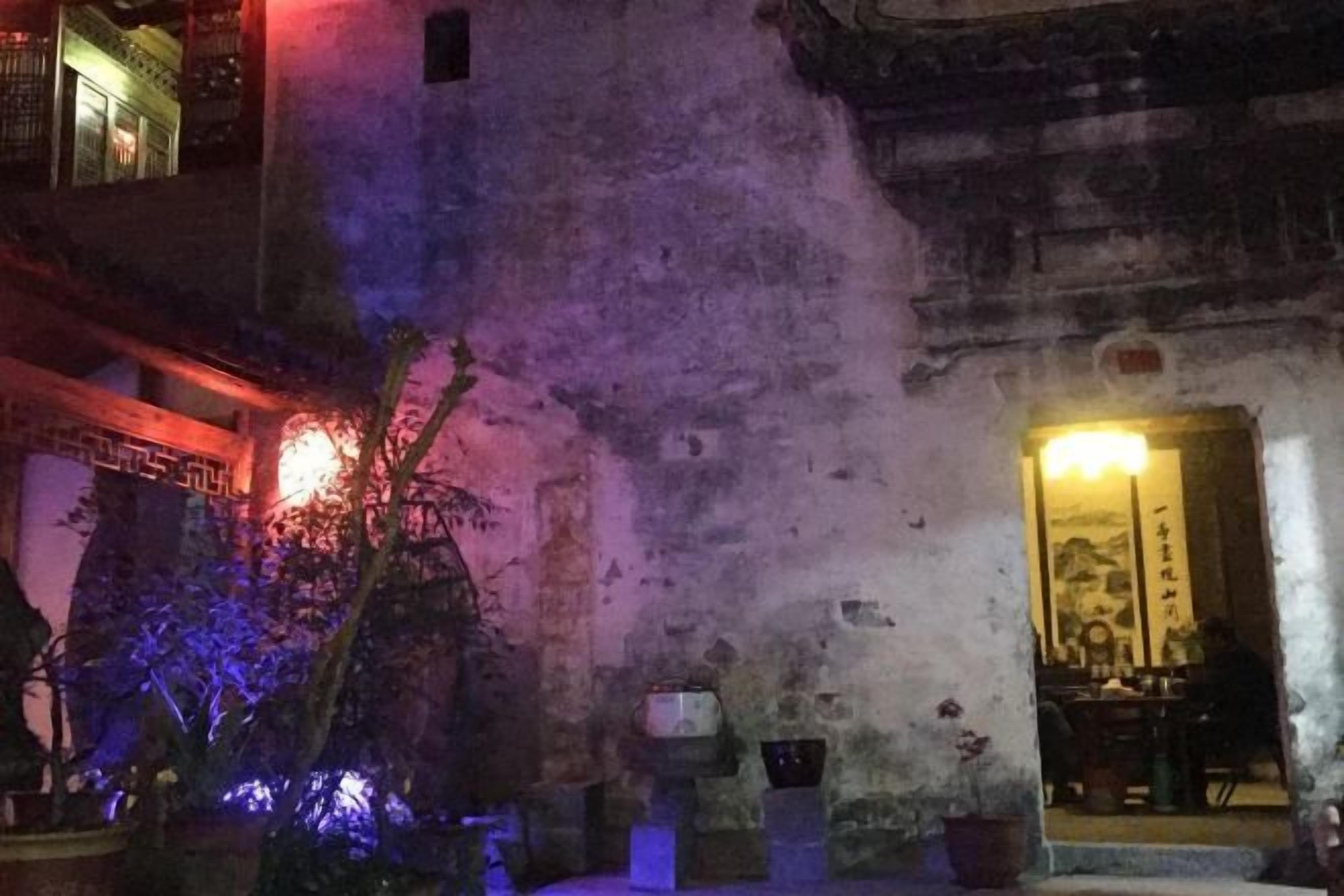 A historic building with traditional architecture, a courtyard with plants, and a well-lit entrance.