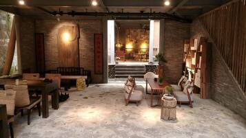 A cozy room with a stone floor, wooden furniture, and a staircase leading to a dining area.