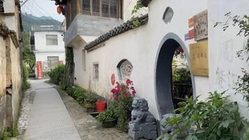 A narrow alleyway with traditional architecture, stone statues, and potted plants.