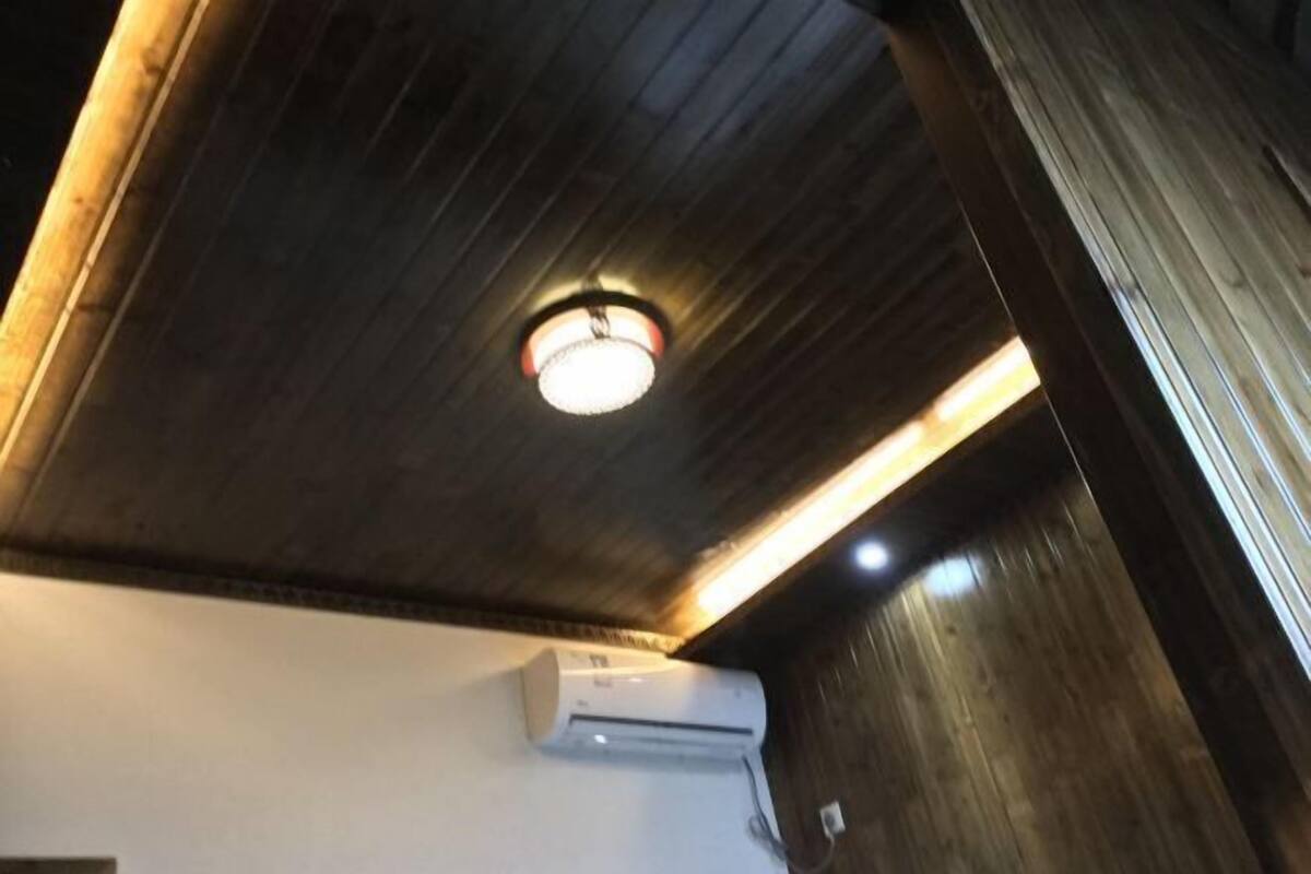 A room with a wooden ceiling, a ceiling light, and an air conditioning unit mounted on the wall.