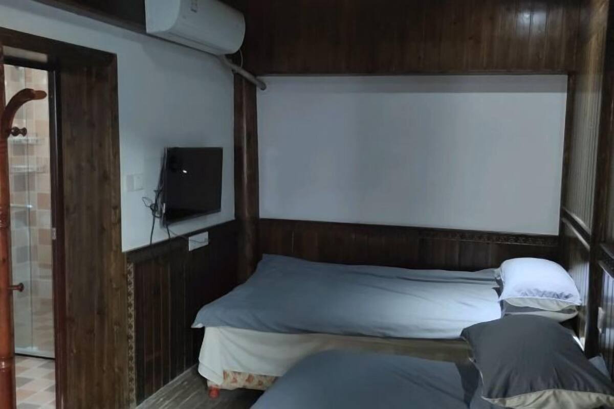 A small, compact room with two beds, a television, and a wooden door.