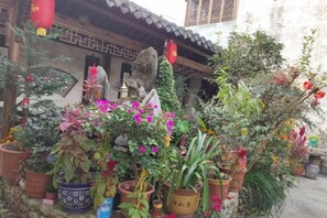 A traditional building with a tiled roof and a courtyard filled with various potted plants and flowers. - Bishan Zhoujiayuan Farmhouse (Yi County)